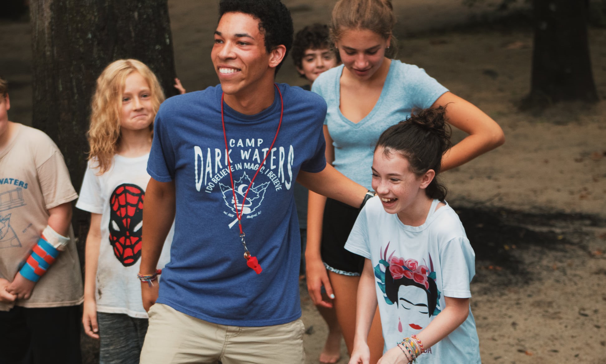 Summer camp leader putting his hand on the shoulder of a child and smiling, at a summer camp in the woods