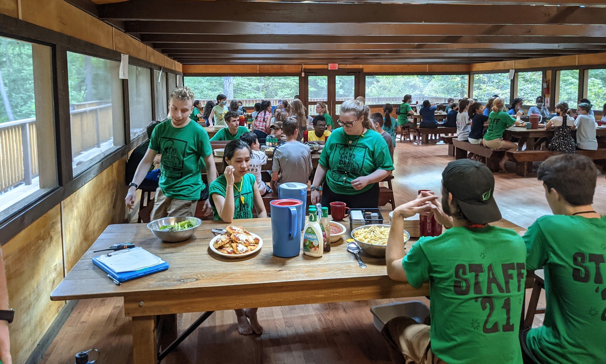 Staff and campers eating in groups at a dining hall at a summer camp